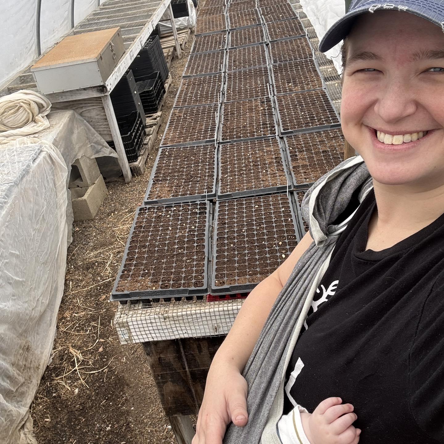 Image of a farmer in her greenhouse with seed trays in the background